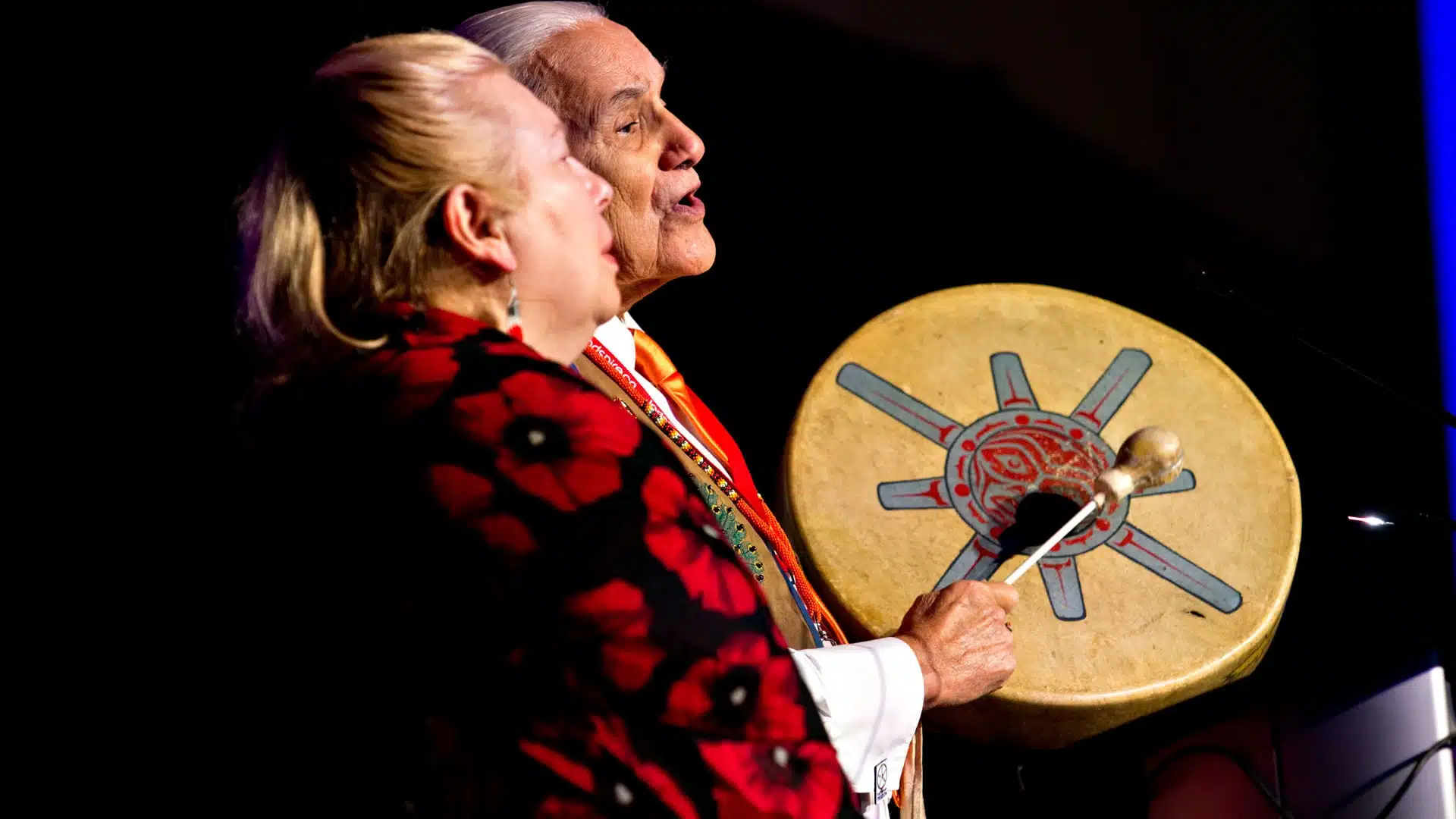 Two Indigenous elders singing with a hand drum.