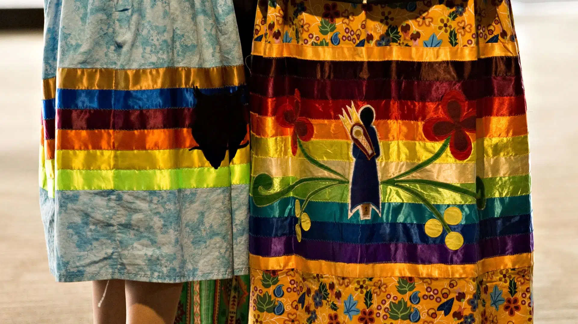 Two people wearing traditional Indigenous Ribbon Skirts.